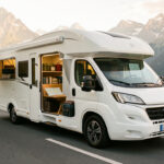 Camping-car moderne prêt à partir sur une route panoramique de montagne, avec des équipements soigneusement rangés et une lumière matinale chaleureuse.