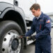 Un jeune homme en formation de conducteur routier inspecte attentivement un camion moderne dans la cour d’un centre de formation.