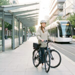 Une jeune femme attend calmement un tramway moderne avec son vélo dans un environnement urbain contemporain et serein.