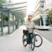 Une jeune femme attend calmement un tramway moderne avec son vélo dans un environnement urbain contemporain et serein.