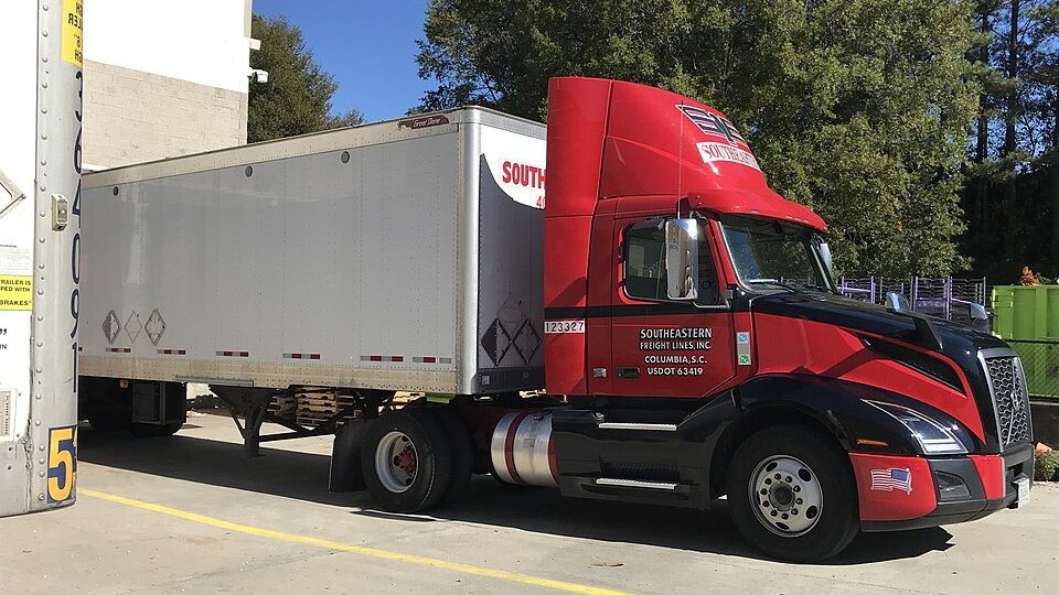 Tracteur routier rouge attelé à une semi-remorque dans une cour de quai